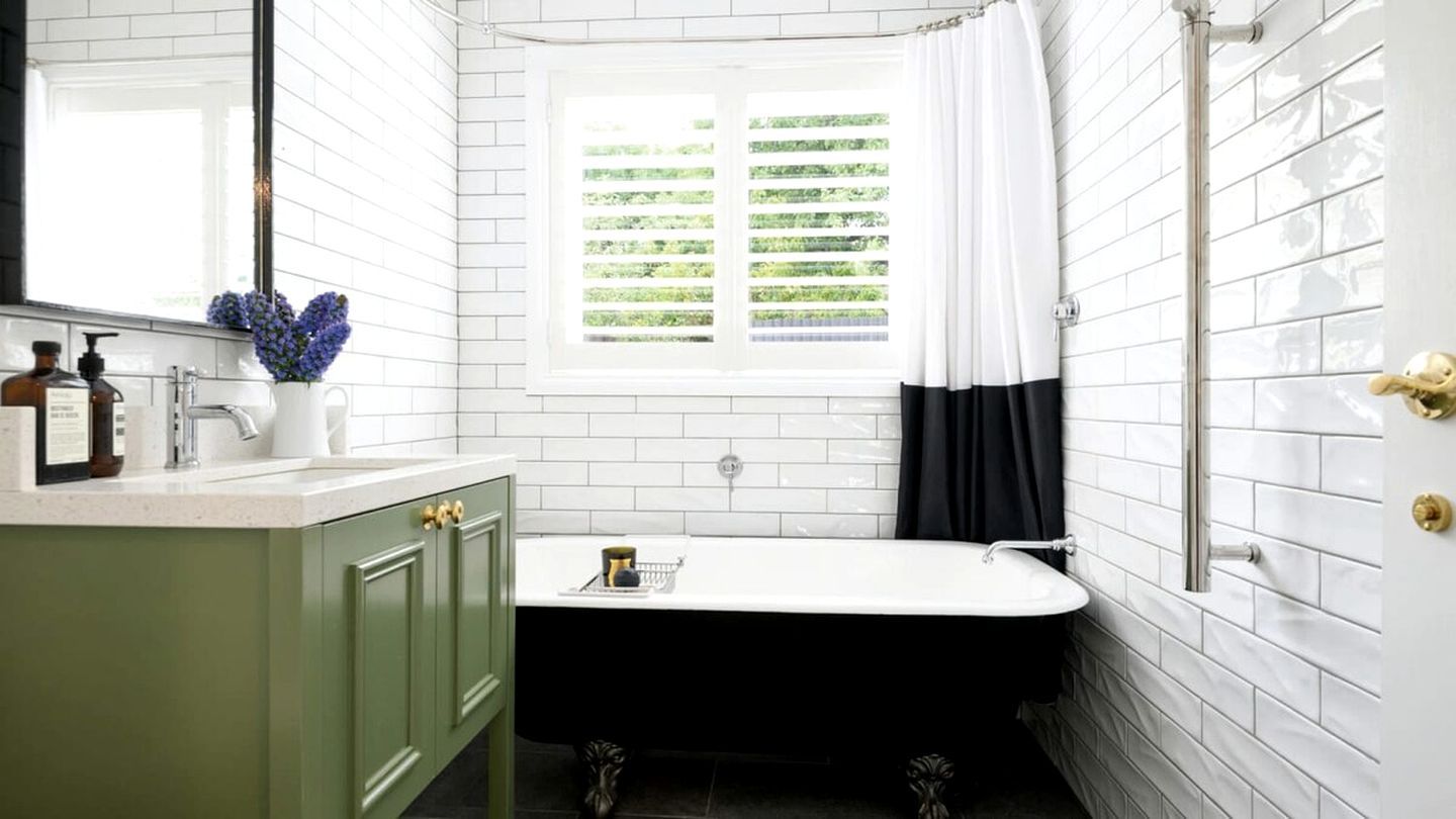 Un bagno con una vasca da bagno bianca, mobili verdi, una finestra con persiane e una tenda da doccia.