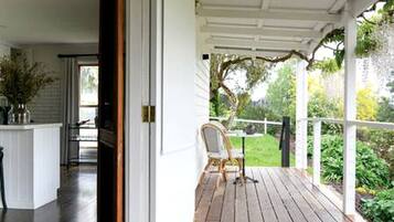 A wooden deck with a chair, a white railing, and a view of a garden.