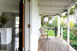 Eine Holzterrasse mit einem Stuhl, einem weißen Geländer und Blick auf einen Garten.