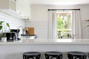 A modern kitchen with white tiled walls, a black countertop, and a window with white curtains.