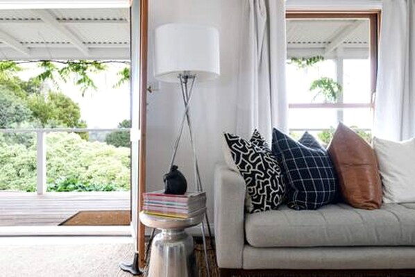 A room with a sofa, a lamp, and a view of greenery outside.