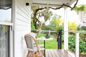A covered porch with wicker chairs, a small round table, and a hanging plant.