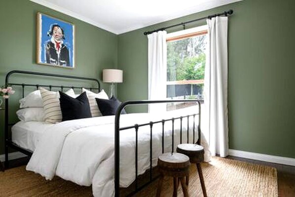 A bedroom with a bed, a nightstand, a window with curtains, and a painting on the wall.