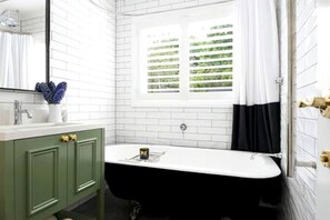 Ein Badezimmer mit einer freistehenden Badewanne, einem Waschbecken mit Spiegel und einem Fenster mit Jalousien.
