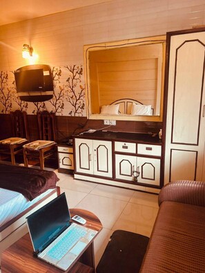 A room with a bed, a desk with a laptop, a TV mounted above the bed, a wardrobe, and a mirror.