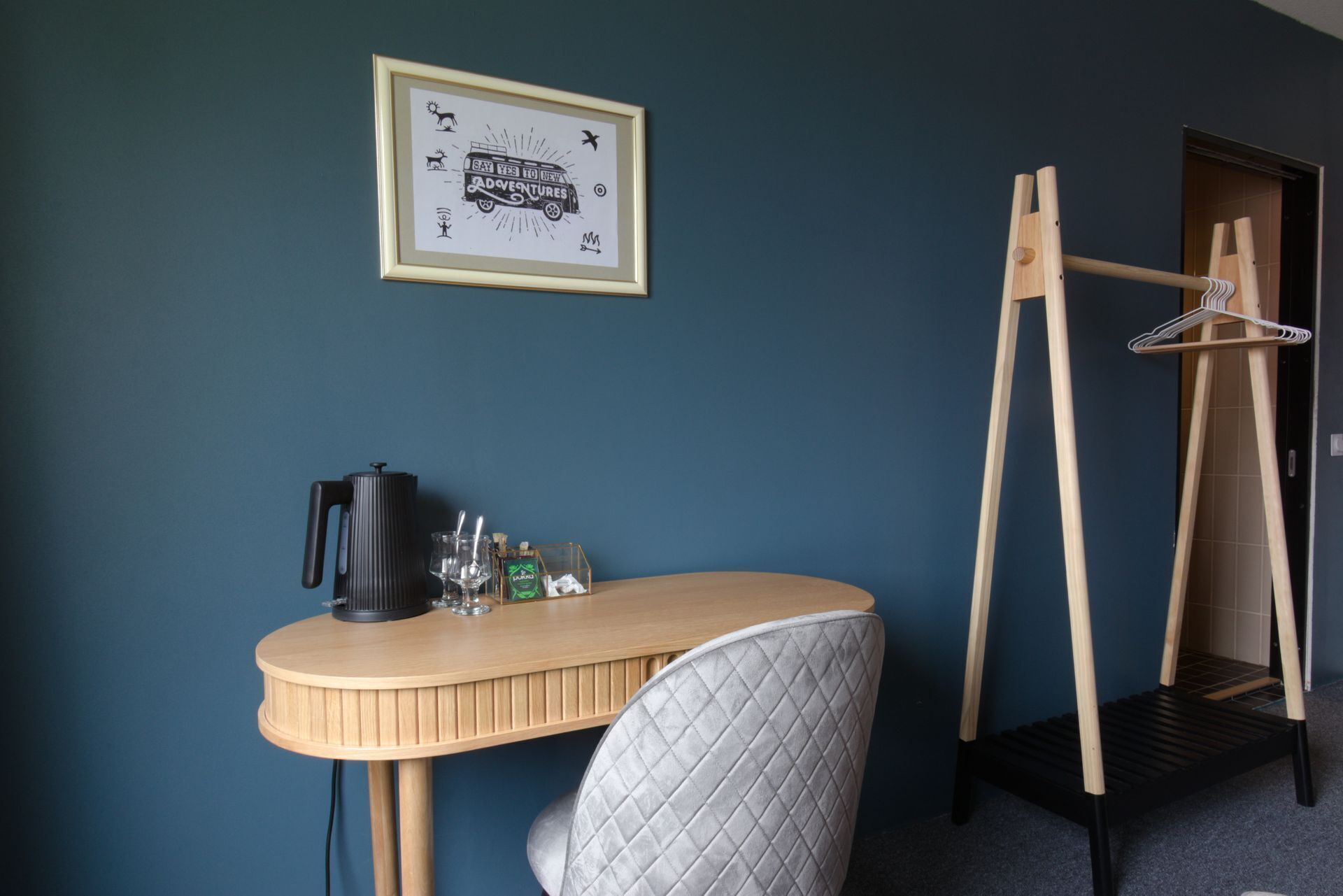 Una habitación con un escritorio, una silla, un perchero y un cuadro en la pared.