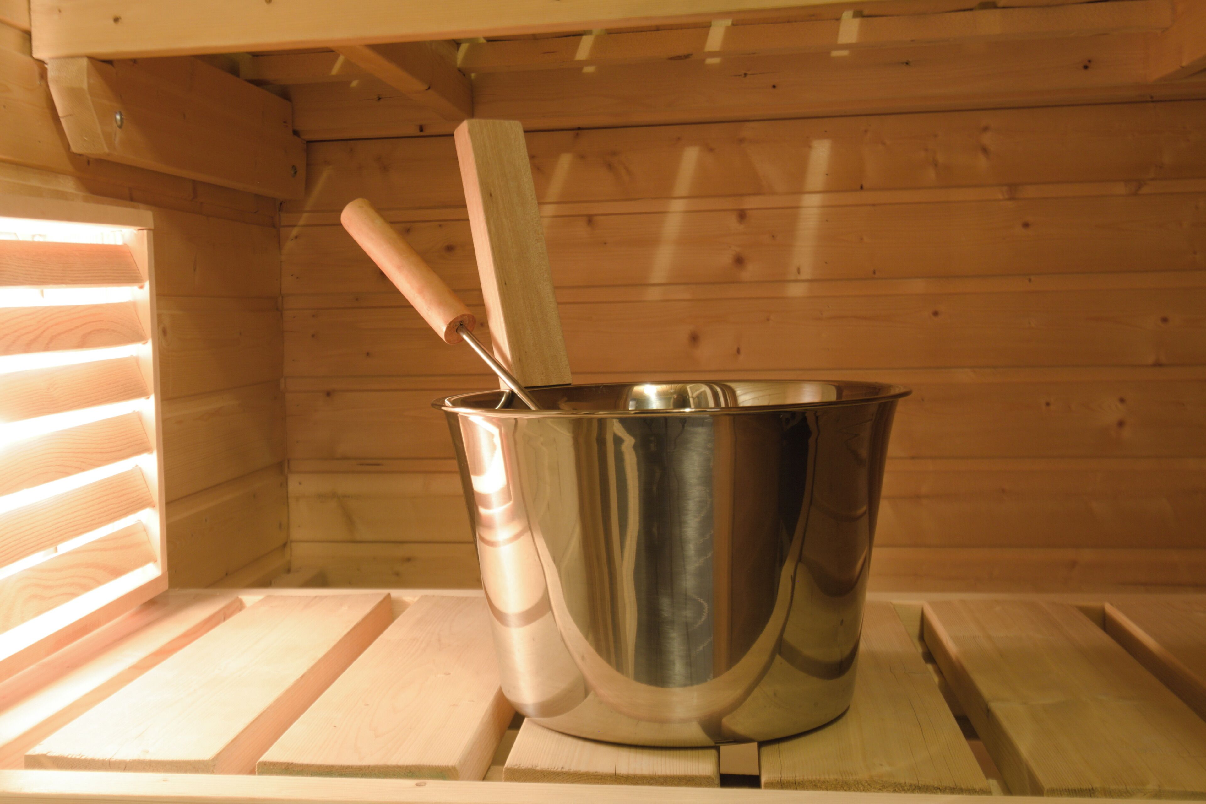 Un cubell metàl·lic amb un mànec de fusta sobre una plataforma de fusta dins una cabana.
