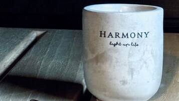 Ett ljus med texten ”HARMONI” och ”sprid ljus i livet”, placerat på en träyta med utspridda stenar.
