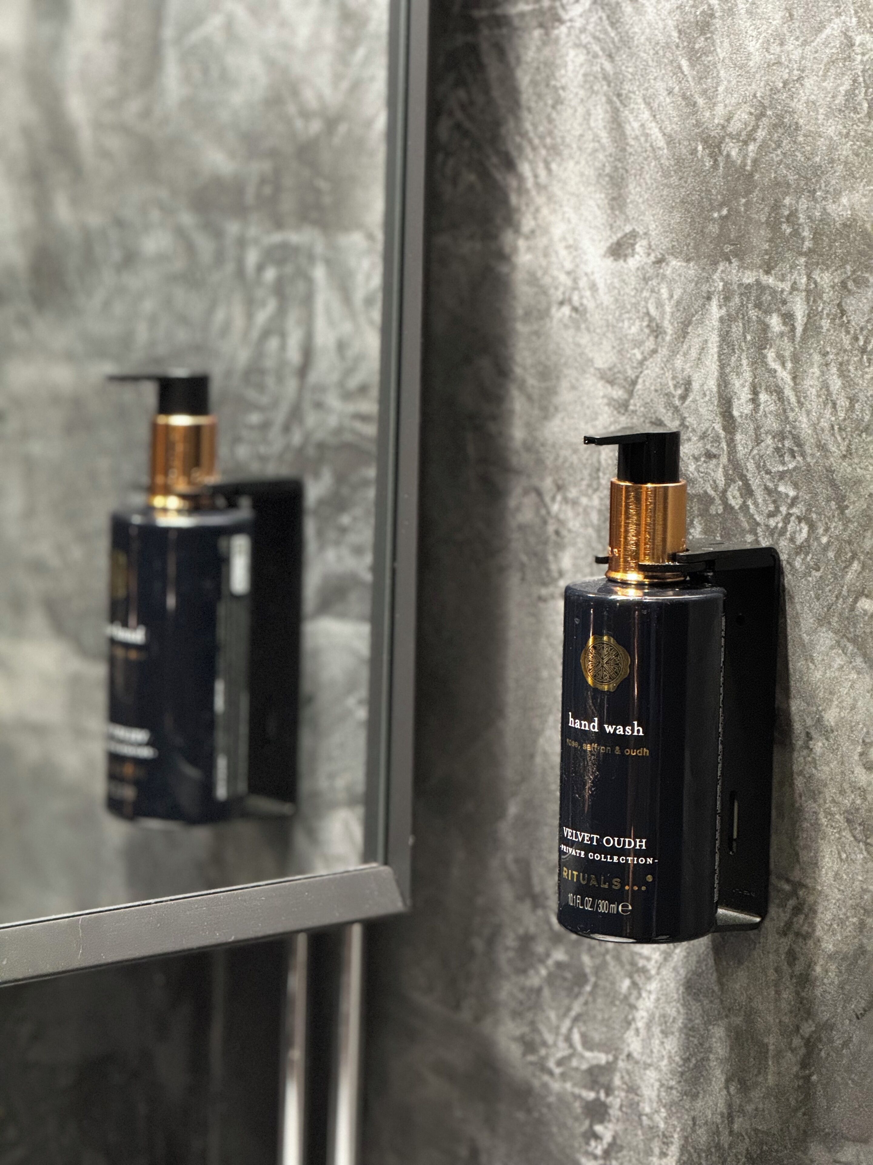 A bathroom with a hand wash dispenser mounted on a textured wall.