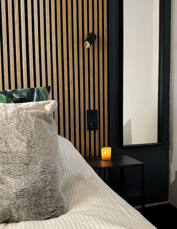 Un dormitorio con cama, mesita de noche con vela, altavoz en la pared y espejo.