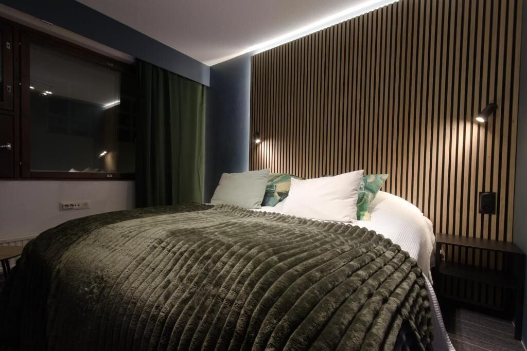 A modern bedroom with a large bed, a wooden slat wall, and a window with curtains.