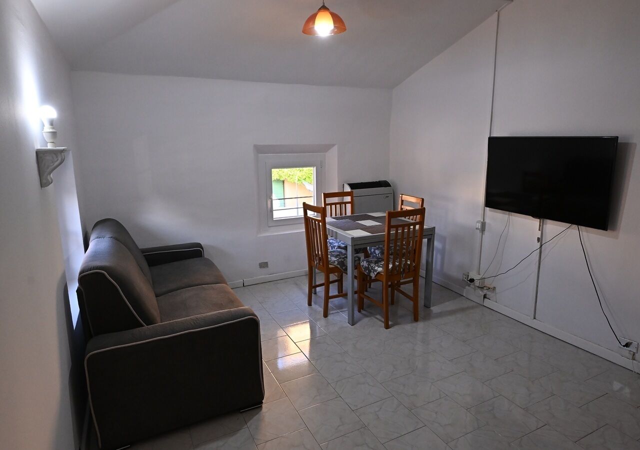 A living room with a sofa, dining table, chairs, a flat-screen TV, and a window.