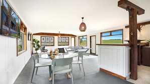 Een ruime kamer met een ronde tafel, stoelen, een tafeltennistafel en grote ramen met uitzicht op de omgeving.