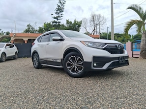 A white SUV parked on a gravel surface with a building and trees in the background. - Airport Oasis 10 min From Las Americas (Santo Domingo Este)