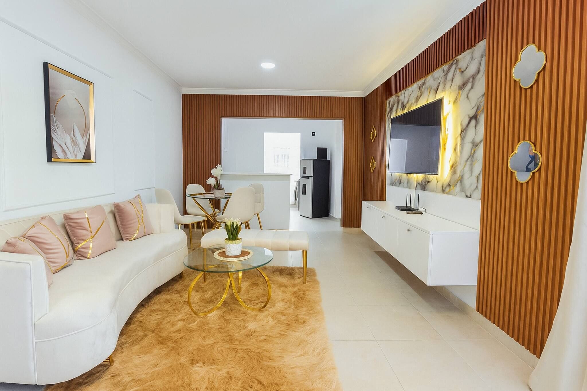 A modern living room with a white sofa, a glass coffee table, and a TV mounted on a marble wall.