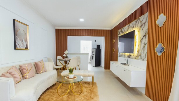 A modern living room with a white sofa, a glass coffee table, and a TV mounted on a marble wall. - Airport Oasis 10 min From Las Americas (Santo Domingo Este)