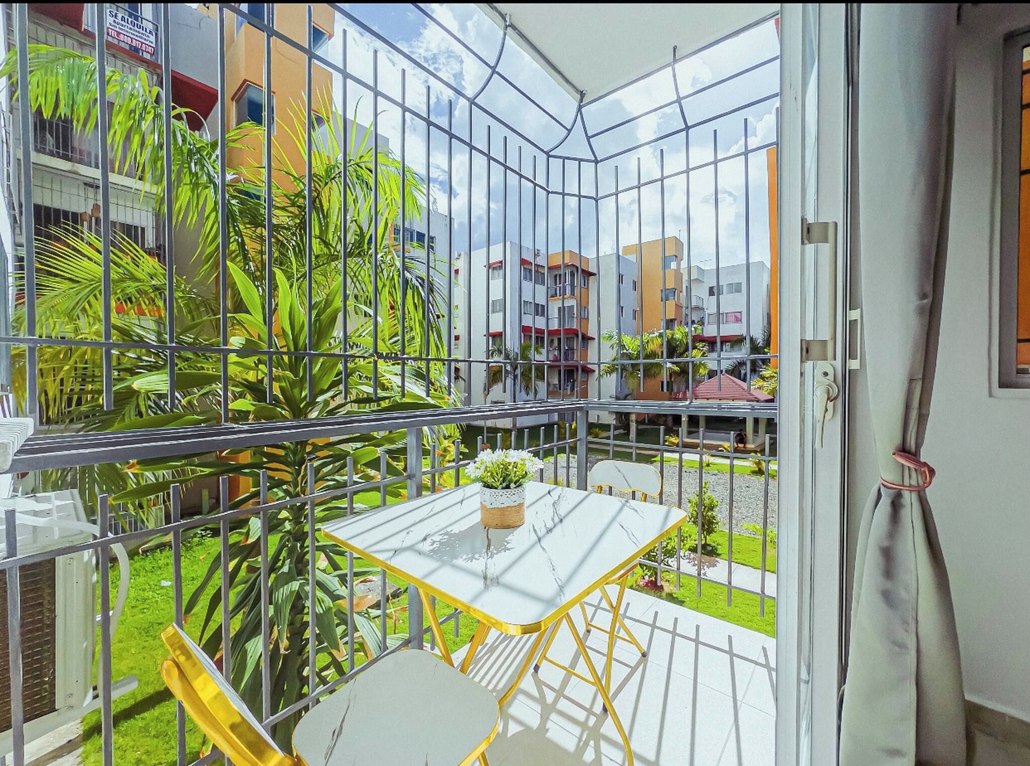 Een balkon met glazen omheining, een tafeltje, een stoel en een plant in een pot.