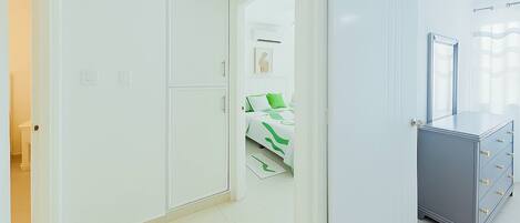 A hallway with a white wardrobe, a bed with green bedding, and a grey dresser with drawers.