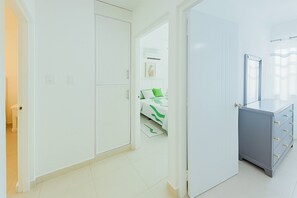 A hallway with a white wardrobe, a bed with green bedding, and a grey dresser with drawers. - Airport Oasis 10 min From Las Americas (Santo Domingo Este)