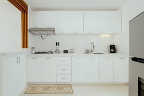 A modern kitchen with white cabinets, a gas stove, a coffee maker, and a built-in oven. - Airport Oasis 10 min From Las Americas (Santo Domingo Este)