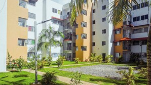 A residential building with multiple balconies, a paved courtyard, and small trees. - Airport Oasis 10 min From Las Americas (Santo Domingo Este)