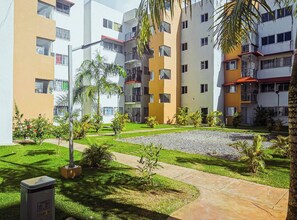 A residential building with multiple balconies, a paved courtyard, and small trees. - Airport Oasis 10 min From Las Americas (Santo Domingo Este)