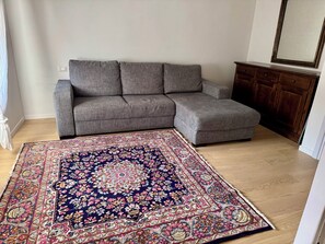 A living room with a grey sectional sofa, a patterned rug, and a wooden cabinet. - Riflesso - Penthouse with queen-size bedrooms and 2 bathrooms (Assisi)