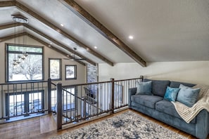 A spacious room with a high ceiling, a staircase with a railing, a grey sofa with cushions, and a patterned rug. - Luxury Black Hills Chalet with Hot Tub Near Mount Rushmore, Keystone SD (Keystone)