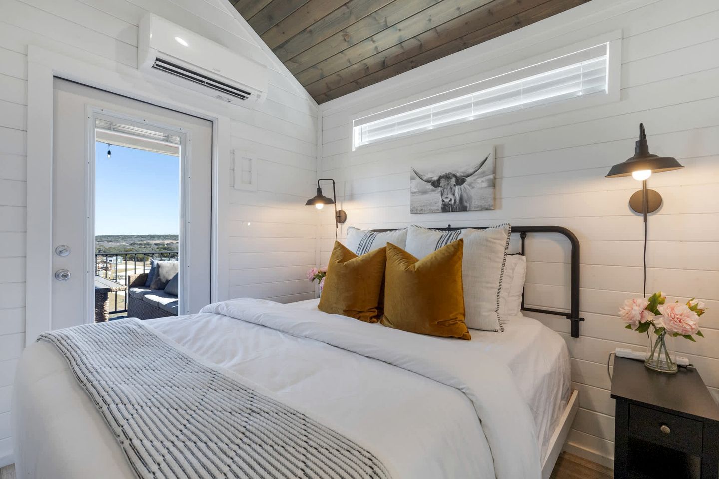 Ein Schlafzimmer mit einem Bett, Nachttischlampen, einem Beistelltisch, einem Fenster und Blick ins Freie.