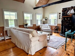 A cozy living room with a sofa, armchair, and a fireplace. - Charming Dog-Friendly Beach House with Fire Pit & Jetted Tub Near Carters Beach in Hancock, Maine (Hancock)