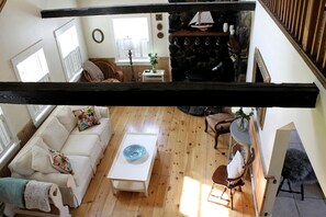 A high-ceilinged living room with a wooden floor, a white sofa, a coffee table, and a fireplace with a ship decoration. - Charming Dog-Friendly Beach House with Fire Pit & Jetted Tub Near Carters Beach in Hancock, Maine (Hancock)