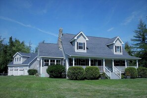 A two-story house with a covered porch, a stone chimney, and a well-maintained lawn. - Charming Dog-Friendly Beach House with Fire Pit & Jetted Tub Near Carters Beach in Hancock, Maine (Hancock)