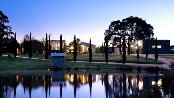 A serene lakeside setting with modern buildings, a pathway, and a small structure near the water.