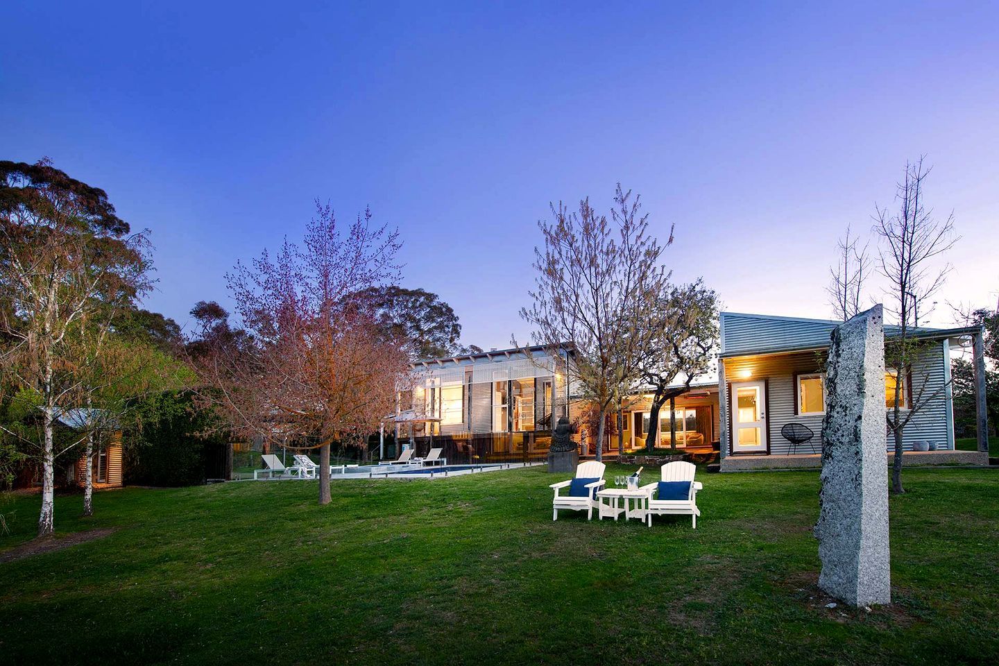 A modern house with a well-maintained lawn, outdoor seating, and a stone sculpture.
