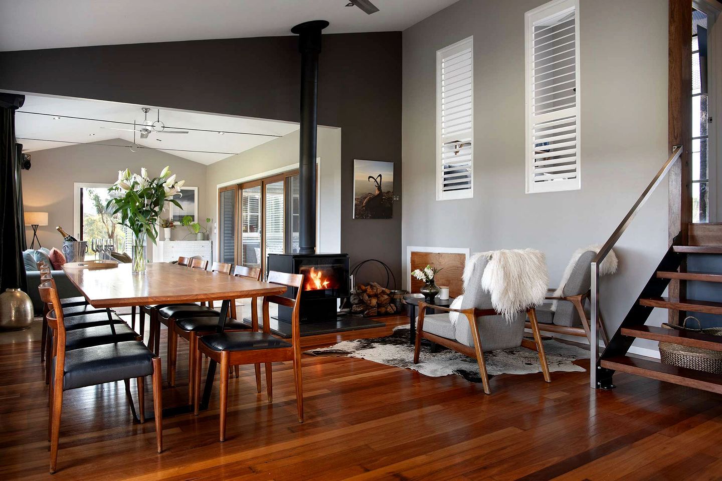A modern living room with a central fireplace, wooden furniture, and a staircase.