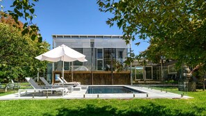 Una casa moderna con piscina, sillas de descanso y una sombrilla.