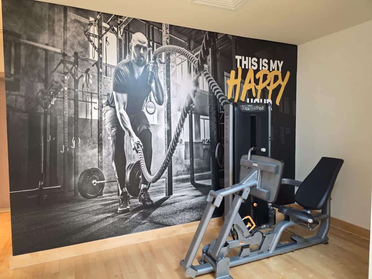 Uma academia com pôster motivacional, equipamentos de musculação e um banco.