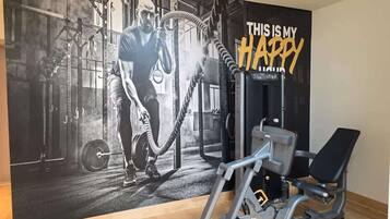 Uma academia com pôster motivacional, equipamentos de musculação e um banco.