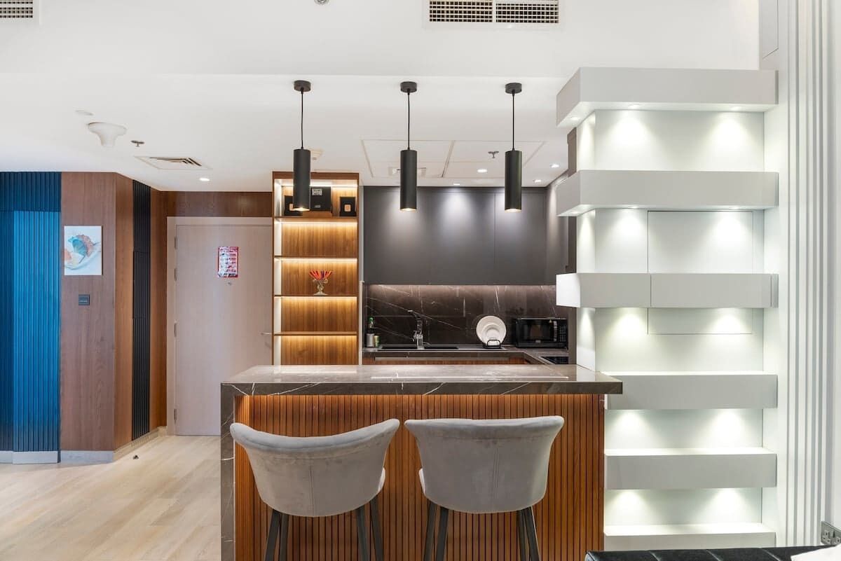 Una cocina moderna con una isla central, iluminación colgante y estantes empotrados.