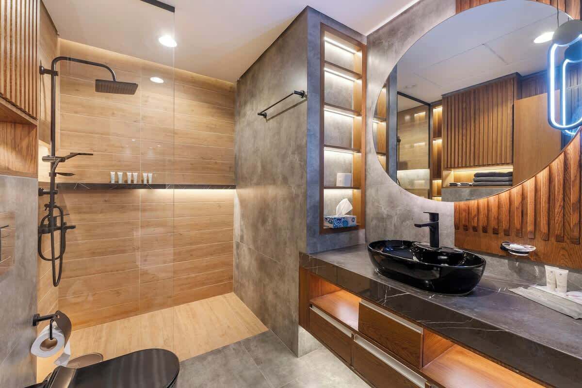 A modern bathroom with a wooden vanity, a black sink, and a large mirror.