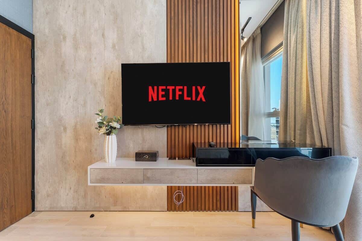 Uma sala de estar moderna com uma televisão de tela plana na parede, um elegante móvel preto abaixo e uma poltrona contemporânea.