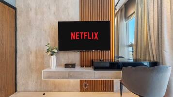 Uma sala de estar moderna com uma televisão de tela plana na parede, um elegante móvel preto abaixo e uma poltrona contemporânea.