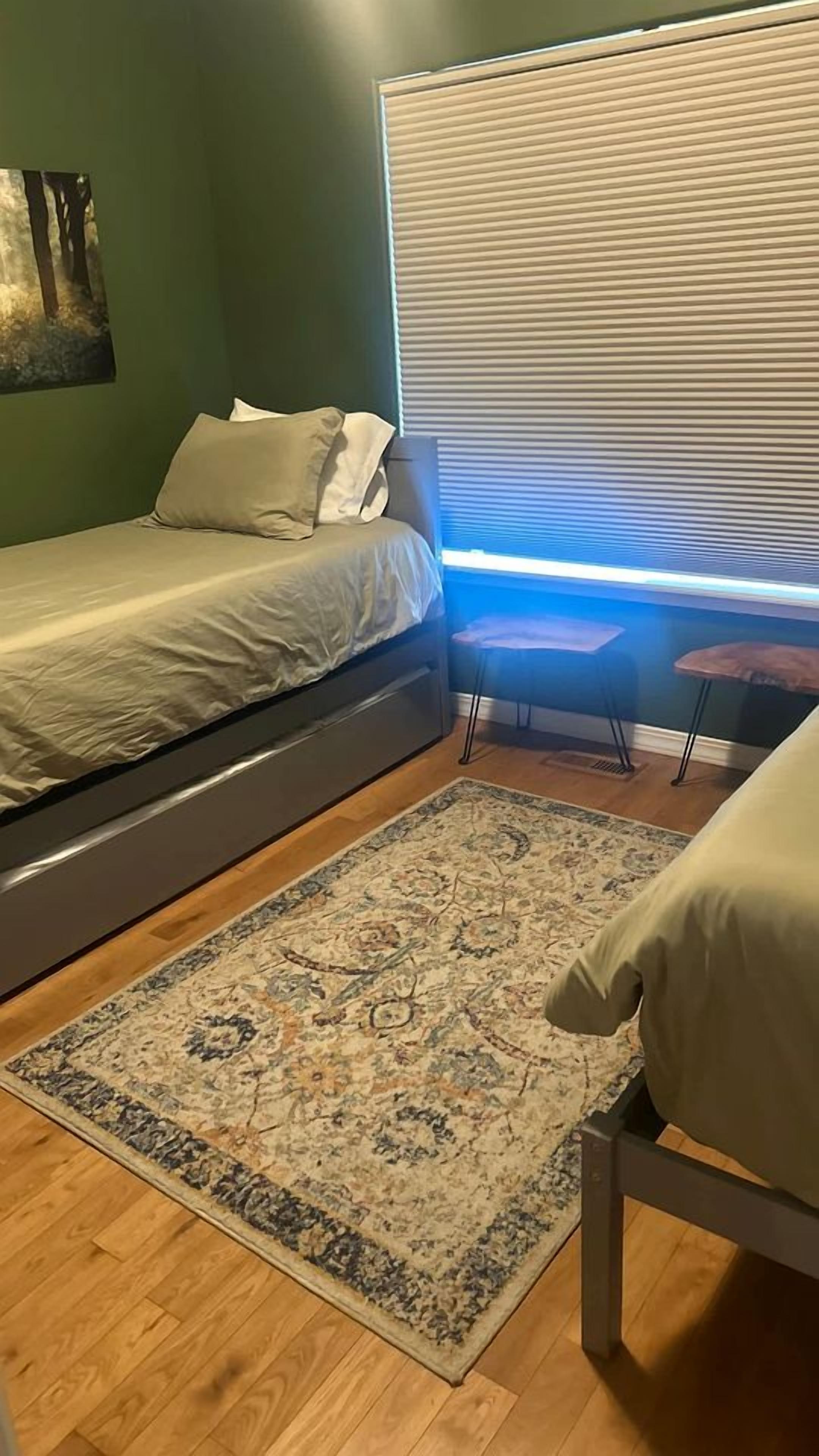 A bedroom with a bed, a bedside table, a rug, and a window with blinds.