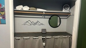 Een slaapkamer met een bed, een plank met opgevouwen handdoeken, een spiegel en een decoratie aan de muur.