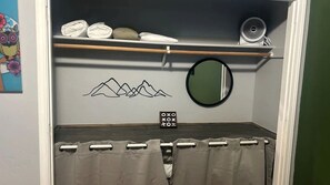 Ein Schlafzimmer mit einem Bett, einem Regal mit gefalteten Handtüchern, einem Spiegel und einer Wanddekoration.