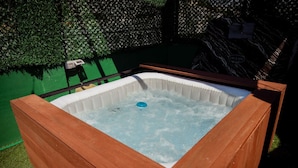 A hot tub with a wooden frame, surrounded by a green hedge and a wooden deck. - Rooftop Apartment w Garden Jacuzzi (Durrës)