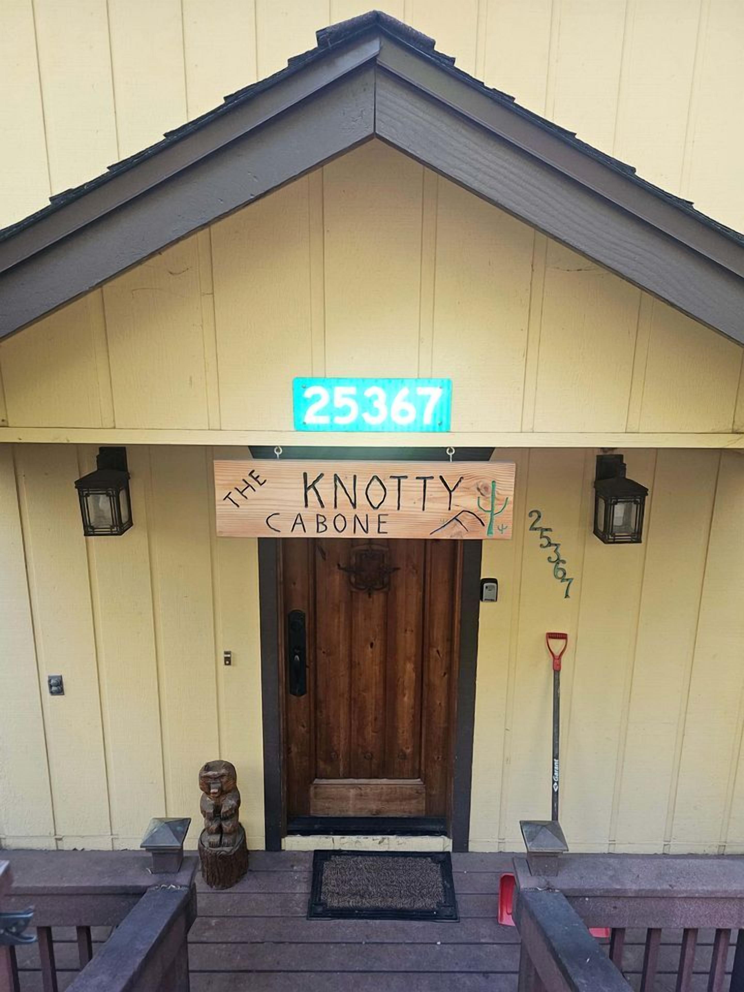Una entrada de edificio con una puerta de madera, un letrero que dice 'The Knotty Cabone' y un buzón.