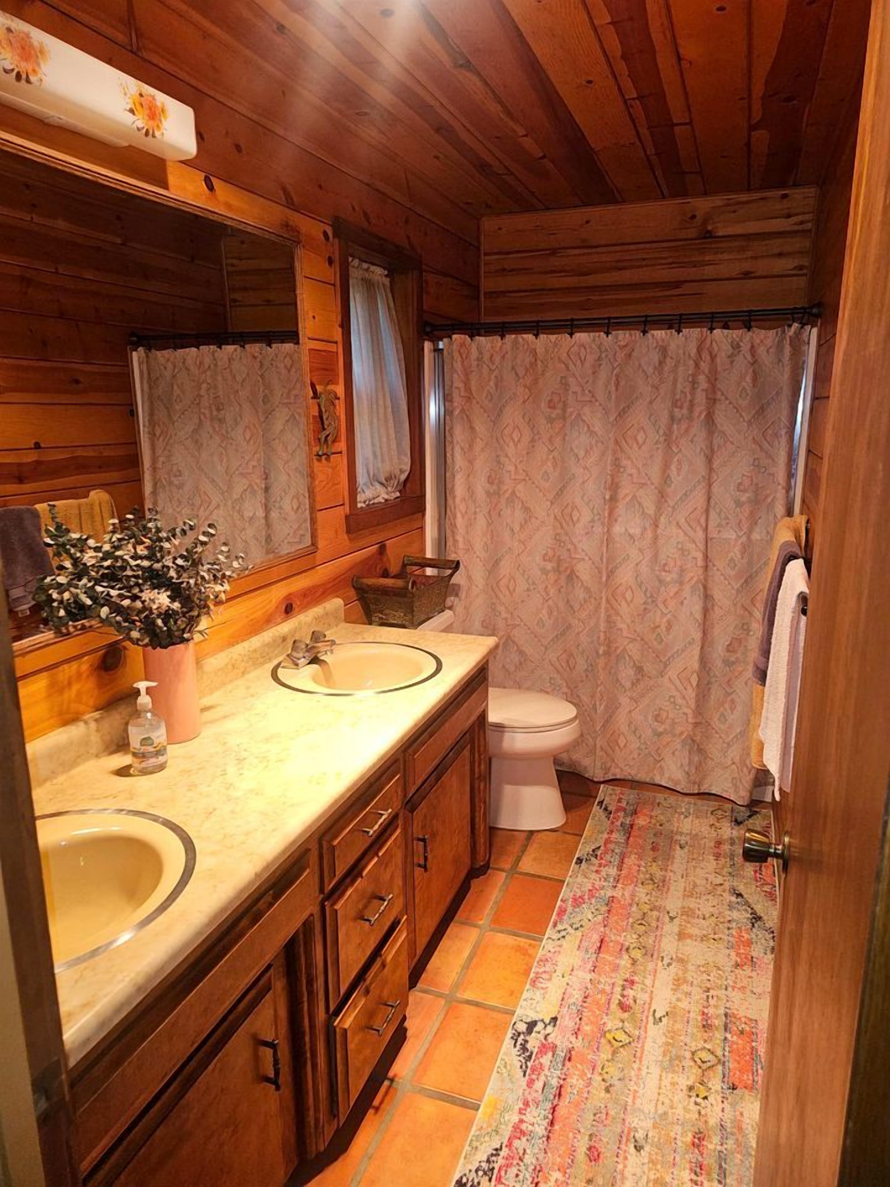 A wooden cabin bathroom with a double sink, toilet, and a shower curtain.