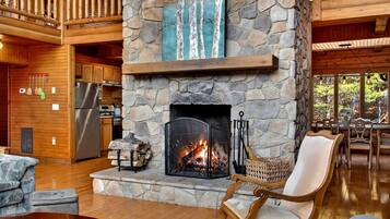 A stone fireplace with a fire, wooden furniture, and a kitchen area.