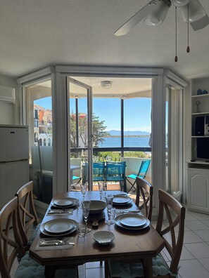 A dining area with a table set for six, a ceiling fan, and a view of the sea through open doors. - Apartment with a view of the pond and mountains, featuring a pool (Le Barcarès)